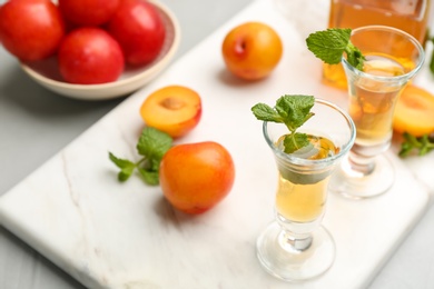 Delicious plum liquor with mint and ripe fruits on light table. Homemade strong alcoholic beverage