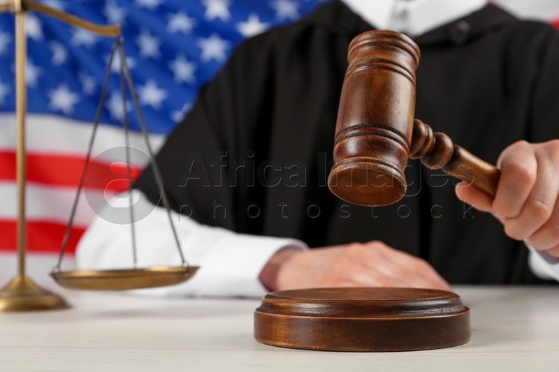 Photo of Judge with gavel at white wooden table against flag of United States, closeup
