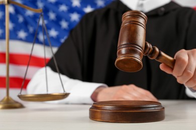 Judge with gavel at white wooden table against flag of United States, closeup