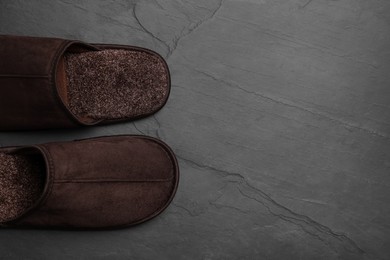 Photo of Pair of brown slippers on dark grey floor, top view. Space for text