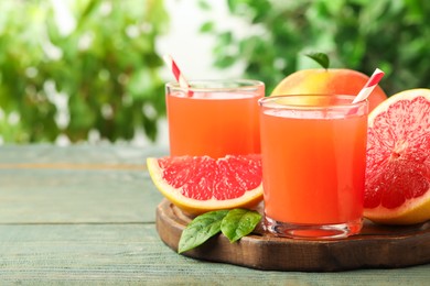 Glasses of delicious grapefruit juice on wooden table against blurred background, space for text