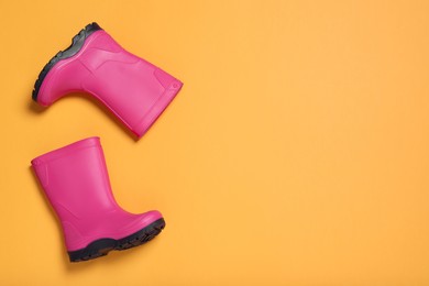 Pair of bright pink rubber boots on orange background, top view. Space for text
