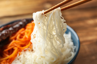 Chopsticks with tasty cooked rice noodles over bowl, closeup