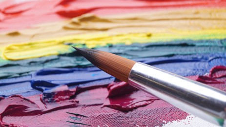 Photo of Brush on artist's palette with colorful mixed paints, closeup