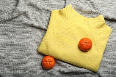 Photo of Yellow warm sweater with tangerines on grey plaid, flat lay. Space for text