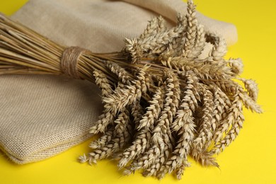 Photo of Bunch of wheat and sack bag on yellow background, closeup