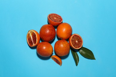 Many ripe sicilian oranges and leaves on light blue background, flat lay