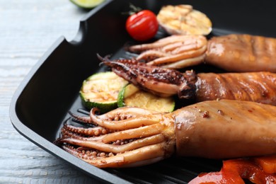 Tasty grilled squids with vegetables served on grey wooden table, closeup