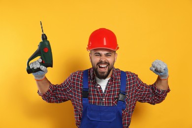 Emotional worker in uniform with power drill on yellow background