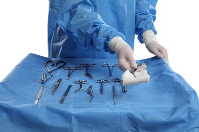 Doctor holding medical forceps with pad near table of different surgical instruments on light background, closeup