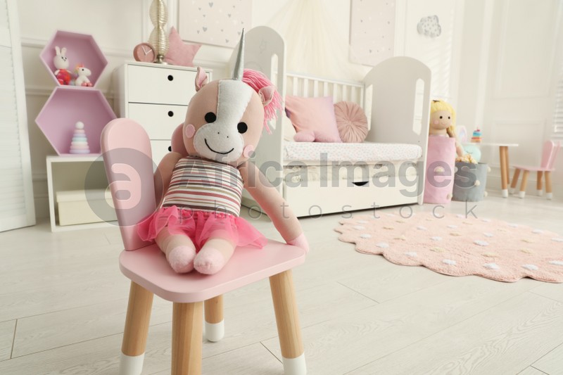Photo of Cute unicorn toy on chair in baby room, space for text. Interior design