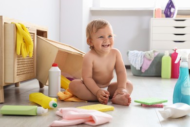 Cute baby surrounded by cleaning supplies at home. Dangerous situation