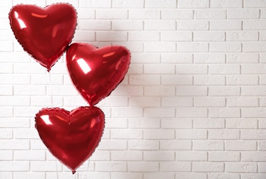 Red heart shaped balloons near white brick wall, space for text. Valentine's Day celebration