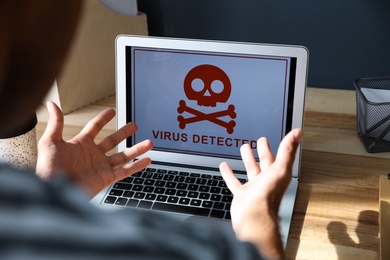 Man in front of laptop with warning about virus attack at workplace, closeup