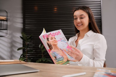 Happy woman reading magazine at workplace in office