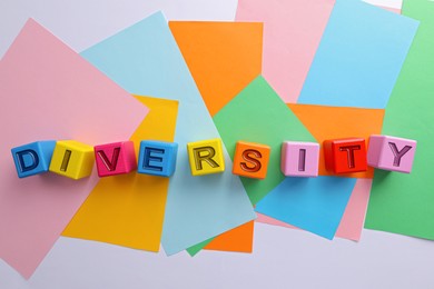 Word Diversity made of cubes with letters and colorful paper sheets on white background, flat lay