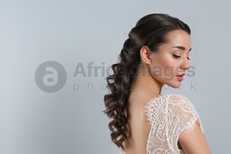 Young bride with beautiful wedding hairstyle on light grey background. Space for text