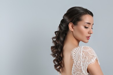 Young bride with beautiful wedding hairstyle on light grey background. Space for text