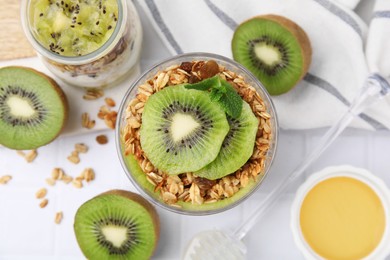Photo of Delicious dessert with kiwi, muesli and fresh cut fruits on white table, flat lay