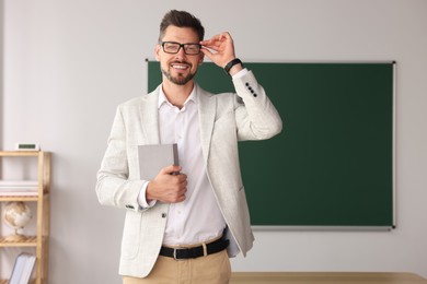 Photo of Happy teacher with glasses and book in classroom