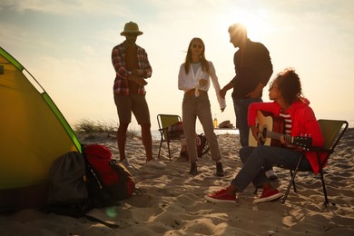 Friends having party near camping tent on sandy beach
