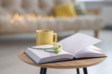 Photo of Yellow mug, open book and eustoma flower on wooden table in living room