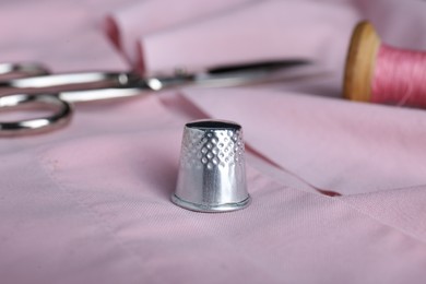 Photo of Silver thimble on pink cloth, closeup. Sewing accessory