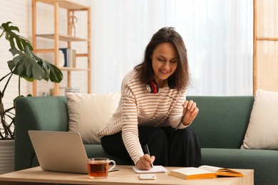 Woman with modern laptop learning on sofa at home