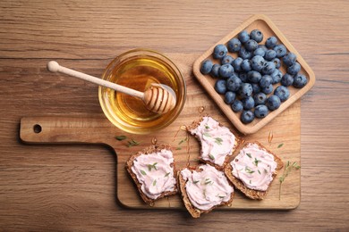Tasty sandwiches with cream cheese, honey and thyme on wooden table, flat lay