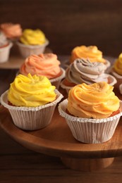 Tasty cupcakes with cream on wooden stand, closeup