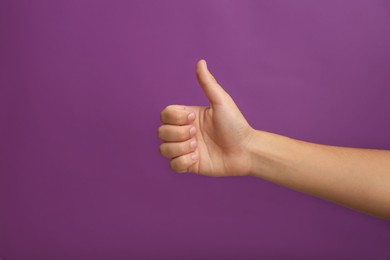 Teenage boy showing thumb up on purple background, closeup