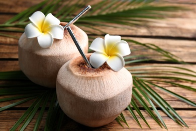 Fresh coconuts with drinking straw and flowers on wooden table, closeup