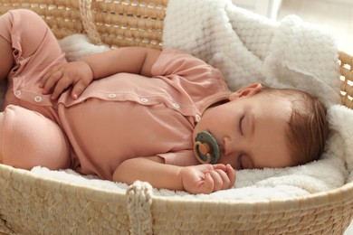 Cute little baby with pacifier sleeping in wicker crib at home