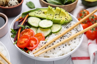 Photo of Delicious poke bowl with vegetables, avocado and mesclun on white table, closeup