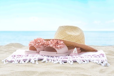 Photo of Blanket with slippers, straw hat and seashell on sand near sea. Beach accessories