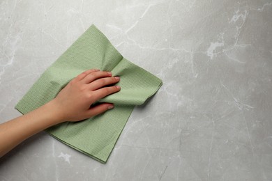 Woman cleaning light grey table with paper towel, top view. Space for text