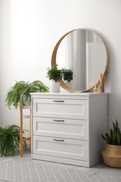 Round mirror and chest of drawers near white wall in room. Modern interior design