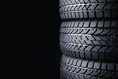 Stacked winter tires on black background, closeup. Space for text