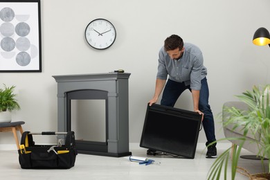 Man installing electric fireplace near wall in room