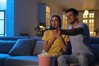 Couple watching movie with popcorn on sofa at night, space for text