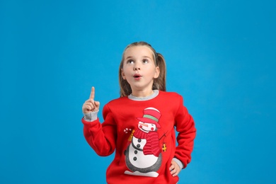 Surprised little girl in Christmas sweater on blue background