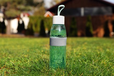 Photo of Glass bottle of fresh water on green grass outdoors