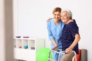 Caretaker helping elderly woman with walking frame indoors