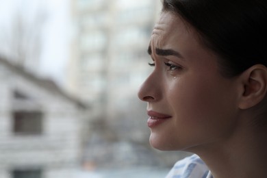 Sad young woman crying near window indoors, closeup with space for text. Loneliness concept