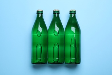 Glass bottles with water on light blue background, flat lay