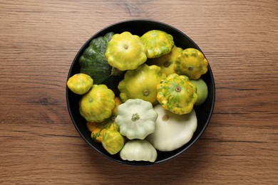 Fresh ripe pattypan squashes in bowl on wooden table, top view