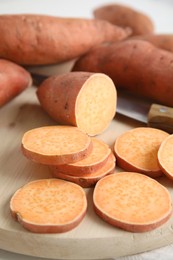 Whole and cut ripe sweet potatoes on wooden board, closeup