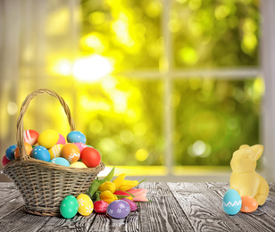 Bright Easter eggs in wicker basket and bunny figure on table indoors