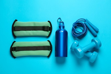 Turquoise weighting agents and sport equipment on light blue background, flat lay