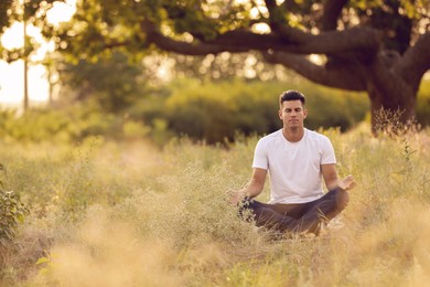 Photo of Man meditating on green grass in park, space for text